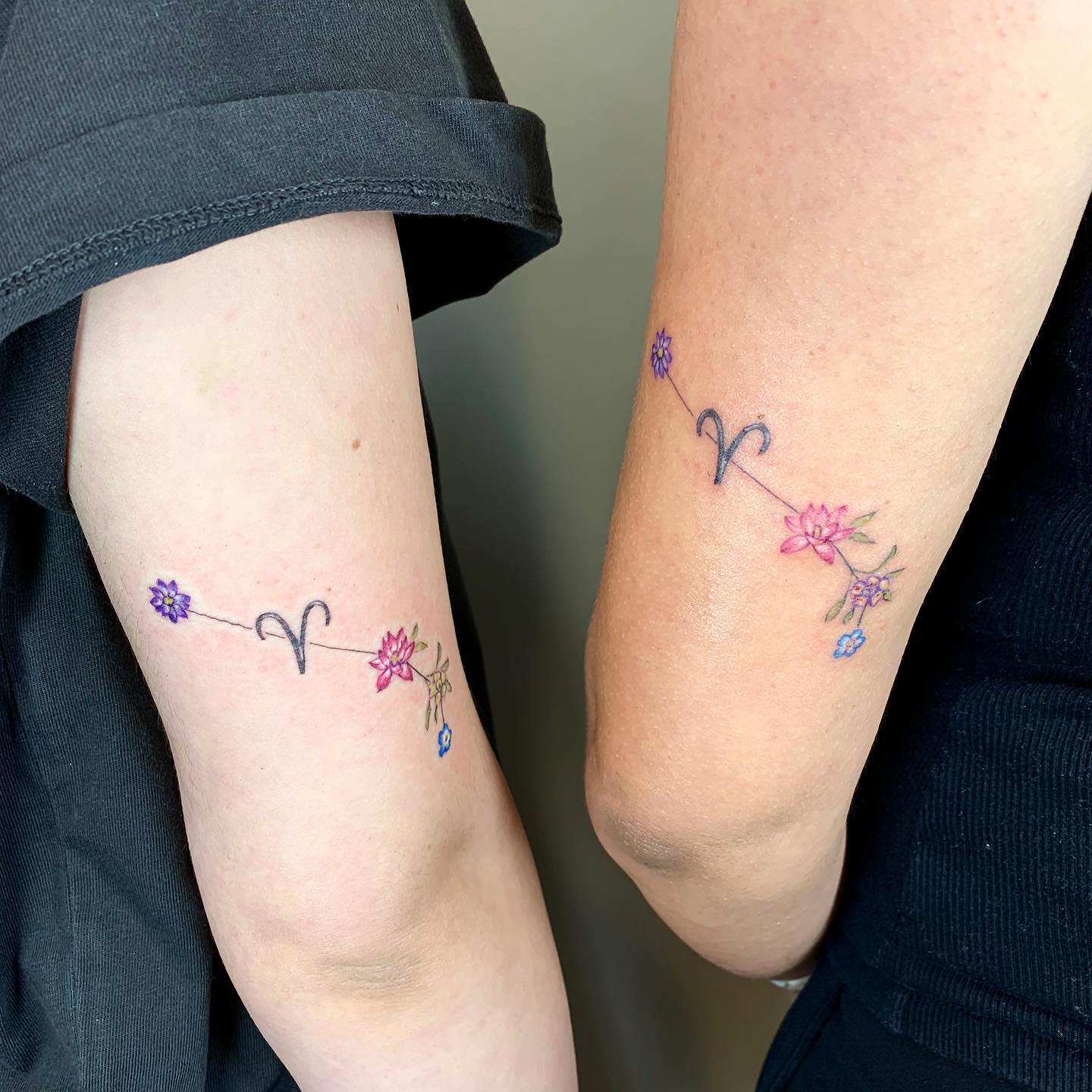 Matching tattoos with colorful flowers and the Aries zodiac symbol, symbolizing a close bond between two individuals